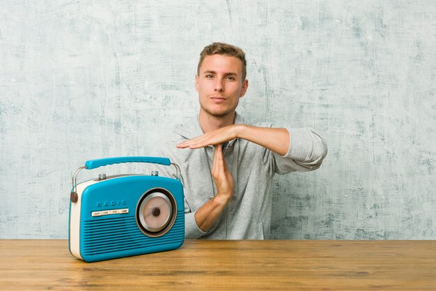 Junger kaukasischer Mann, der zum Radio zeigt eine Zeitüberschreitungsgeste hört.