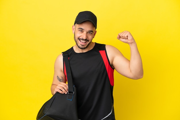 Junger kaukasischer Mann des Sports mit Sporttasche lokalisiert auf gelbem Hintergrund, der einen Sieg feiert