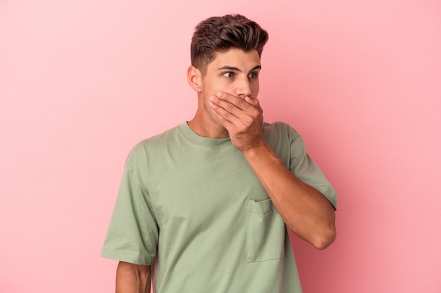 Junger kaukasischer Mann einzeln auf rosafarbenem Hintergrund, der nachdenklich auf einen Kopienraum blickt, der den Mund mit der Hand bedeckt.