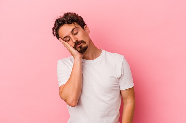 Junger kaukasischer Mann einzeln auf rosafarbenem Hintergrund, der sich langweilt, müde ist und einen entspannten Tag braucht.