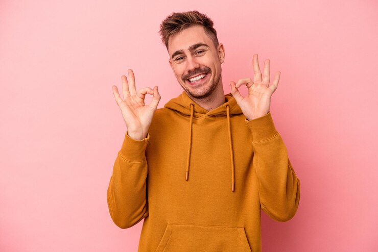 Foto junger kaukasischer mann einzeln auf rosafarbenem hintergrund fröhlich und selbstbewusst, der eine ok geste zeigt.