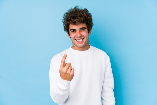 Junger kaukasischer Mann gegen eine blaue Wand lokalisierte das Zeigen mit dem Finger auf Sie, als ob Einladung näher kommen.