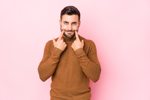 Junger kaukasischer Mann gegen eine rosa Wand isolierte Zweifel zwischen zwei Optionen.