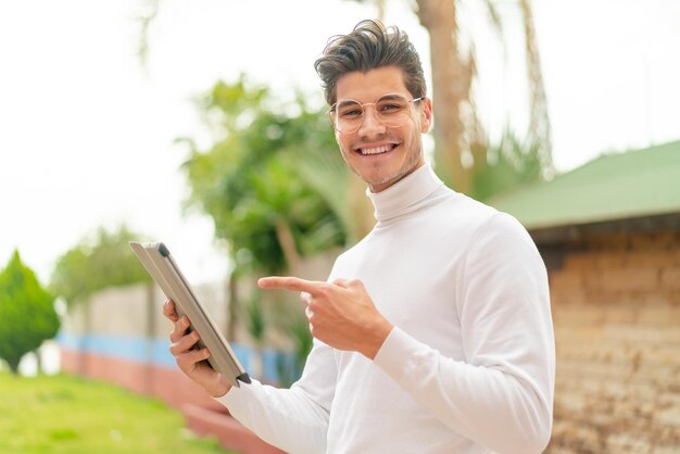 Junger kaukasischer mann im freien, der den tablet-bildschirm mit glücklichem ausdruck berührt