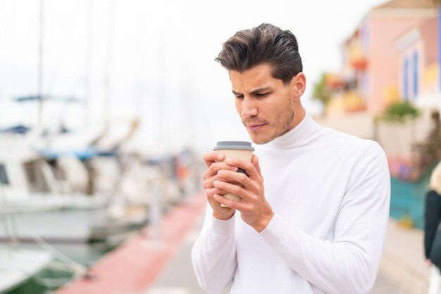 Junger kaukasischer Mann im Freien, der einen Kaffee zum Mitnehmen hält