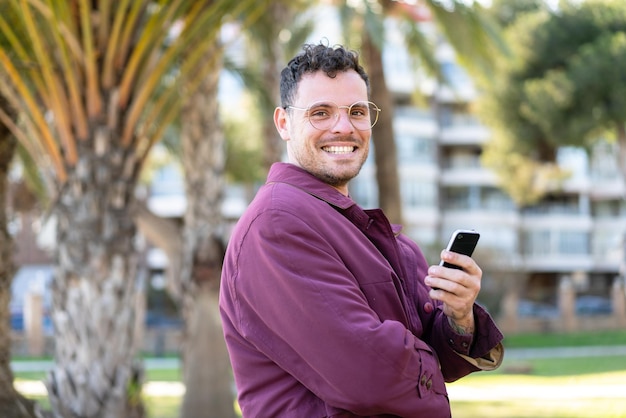 Junger kaukasischer Mann im Freien mit einem Handy und verschränkten Armen