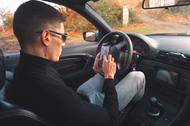 Junger kaukasischer mann innerhalb eines autos unter verwendung eines smartphones