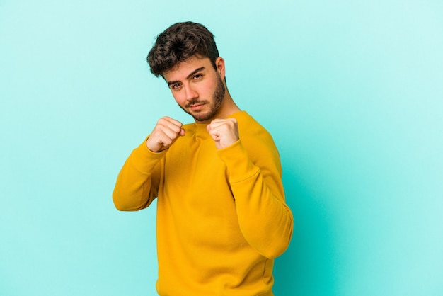 Junger kaukasischer Mann isoliert auf blauem Hintergrund, der einen Schlag wirft, Wut, Kämpfe aufgrund eines Streits, Boxen.