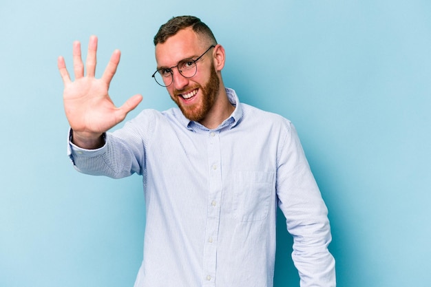 Foto junger kaukasischer mann isoliert auf blauem hintergrund lächelnd fröhlich zeigt nummer fünf mit den fingern
