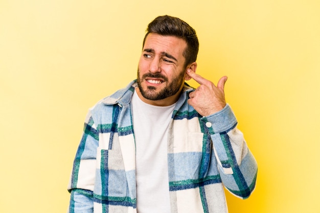 Junger kaukasischer Mann isoliert auf gelbem Hintergrund, der die Ohren mit den Händen bedeckt