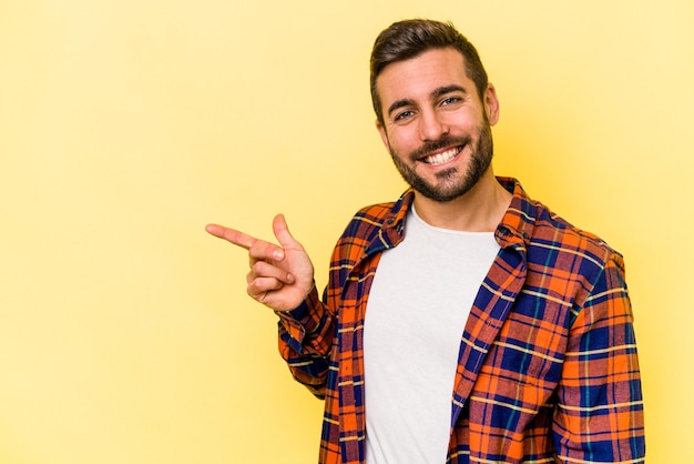 Junger kaukasischer Mann isoliert auf gelbem Hintergrund, der fröhlich lächelt und mit dem Zeigefinger wegzeigt
