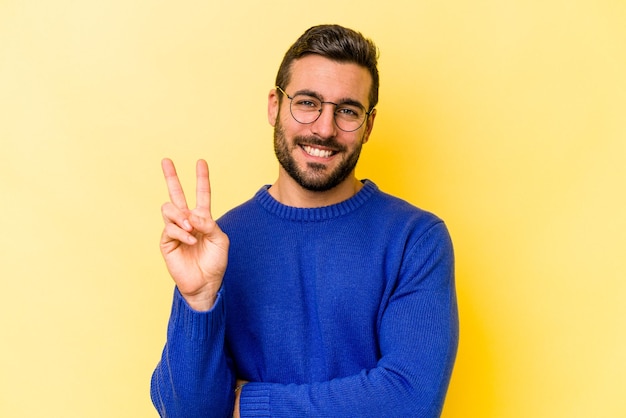 Junger kaukasischer Mann isoliert auf gelbem Hintergrund, der Nummer zwei mit den Fingern zeigt