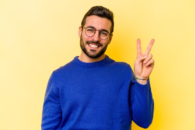 Junger kaukasischer Mann isoliert auf gelbem Hintergrund fröhlich und sorglos mit einem Friedenssymbol mit den Fingern