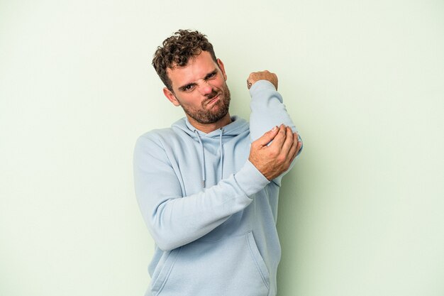 Junger kaukasischer Mann isoliert auf grünem Hintergrund, der Nackenschmerzen aufgrund von Stress hat, massiert und mit der Hand berührt.