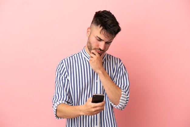 Junger kaukasischer Mann isoliert auf rosa Hintergrund denkt und sendet eine Nachricht