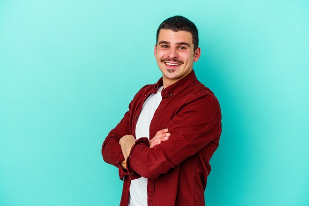Junger kaukasischer Mann lokalisiert auf blauer Wand glücklich, lächelnd und fröhlich.