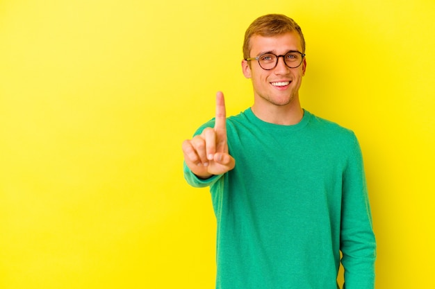 Junger kaukasischer Mann lokalisiert auf gelbem Hintergrund, der Nummer eins mit dem Finger zeigt.