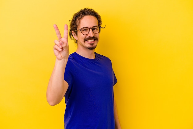 Junger kaukasischer Mann lokalisiert auf gelbem Hintergrund freudig und sorglos, ein Friedenssymbol mit den Fingern zeigend.