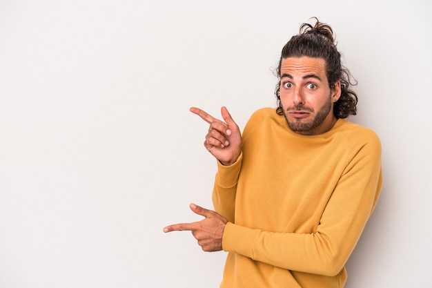 Junger kaukasischer Mann lokalisiert auf grauem Hintergrund schockiert, der mit Zeigefingern auf einen Kopienraum zeigt.