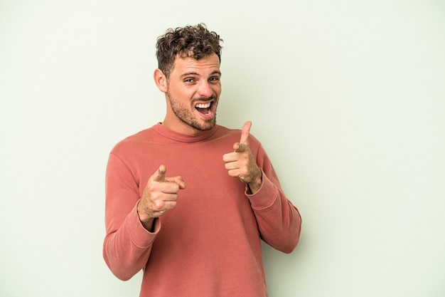 Junger kaukasischer Mann lokalisiert auf grünem Hintergrund, der mit den Fingern nach vorne zeigt.