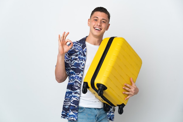 Junger kaukasischer Mann lokalisiert auf Weiß im Urlaub mit Reisekoffer und OK-Zeichen machen