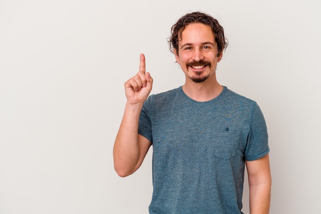 Junger kaukasischer Mann lokalisiert auf weißer Wand, die Nummer eins mit Finger zeigt.