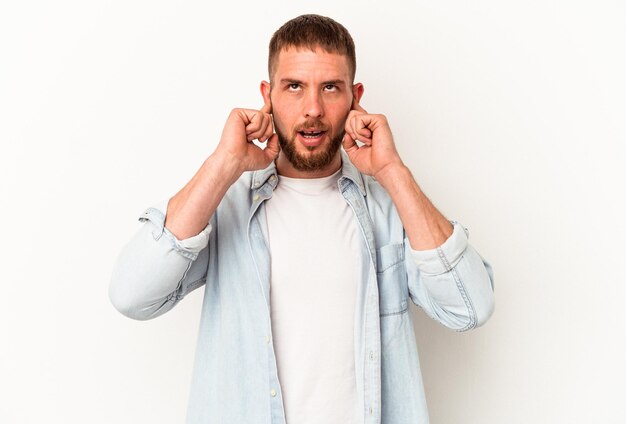 Junger kaukasischer Mann mit Diastema isoliert auf weißem Hintergrund, der die Ohren mit den Fingern bedeckt, gestresst und verzweifelt durch eine laute Umgebung.