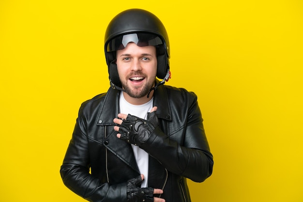 Junger kaukasischer Mann mit einem Motorradhelm, der auf gelbem Hintergrund isoliert ist und viel lächelt