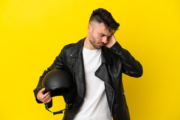 Junger kaukasischer Mann mit einem Motorradhelm isoliert auf gelbem Hintergrund mit Kopfschmerzen