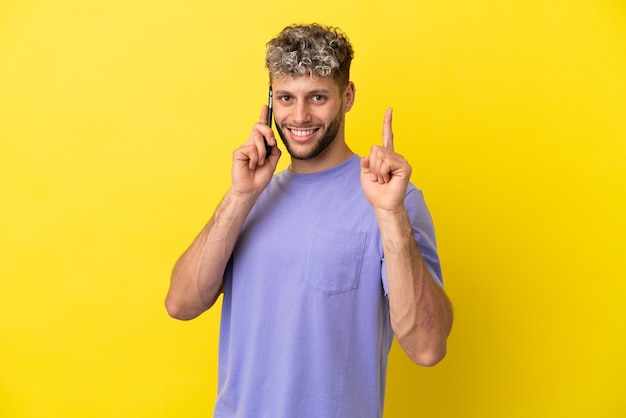 Junger kaukasischer Mann mit Handy isoliert auf gelbem Hintergrund, der einen Finger im Zeichen des Besten zeigt und anhebt