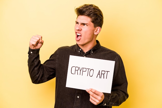 Junger kaukasischer Mann mit Krypto-Art-Plakat isoliert auf gelbem Hintergrund, der nach einem Siegerkonzept die Faust erhebt