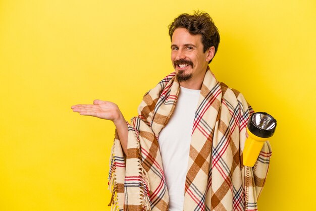 Foto junger kaukasischer mann mit laterne isoliert auf gelbem hintergrund, der einen kopienraum auf einer handfläche zeigt und eine andere hand an der taille hält.