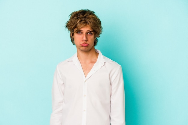 Junger kaukasischer Mann mit Make-up einzeln auf blauem Hintergrund trauriges, ernstes Gesicht, das sich elend und unzufrieden fühlt.