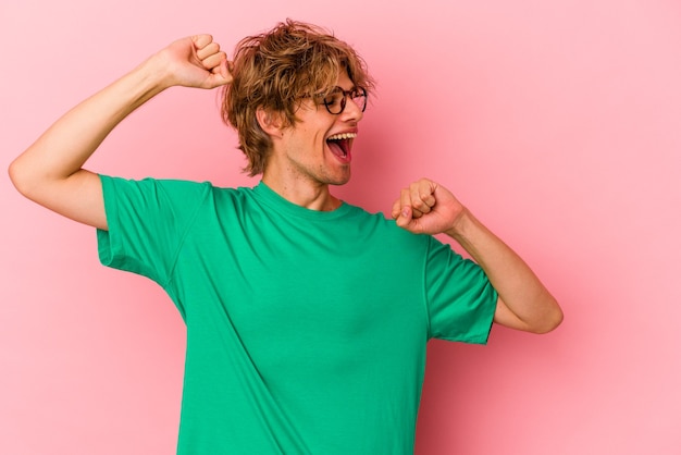 Foto junger kaukasischer mann mit make-up einzeln auf rosafarbenem hintergrund, der einen besonderen tag feiert, springt und hebt die arme mit energie.