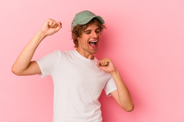 Junger kaukasischer Mann mit Make-up einzeln auf rosafarbenem Hintergrund, der einen besonderen Tag feiert, springt und hebt die Arme mit Energie.