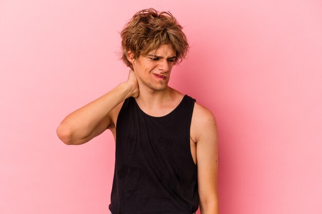 Junger kaukasischer Mann mit Make-up einzeln auf rosafarbenem Hintergrund, der Nackenschmerzen aufgrund einer sitzenden Lebensweise hat.