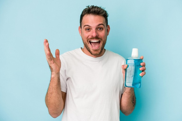 Junger kaukasischer Mann mit Mundwasser isoliert auf blauem Hintergrund, der eine angenehme Überraschung erhält, aufgeregt und die Hände hebt.