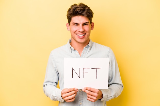 Junger kaukasischer Mann mit NFT-Plakat isoliert auf gelbem Hintergrund lachend und Spaß habend