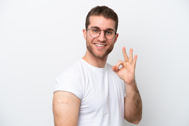 Junger kaukasischer Mann mit Pflaster isoliert auf weißem Hintergrund, der mit den Fingern ein Ok-Zeichen zeigt