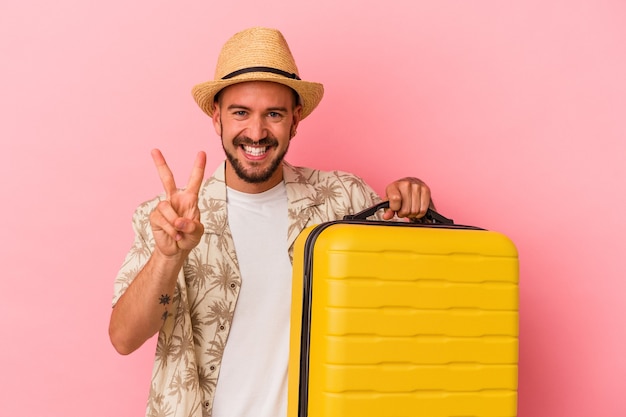 Junger kaukasischer Mann mit Tätowierungen, die einzeln auf rosafarbenem Hintergrund reisen, der Nummer zwei mit den Fingern zeigt.