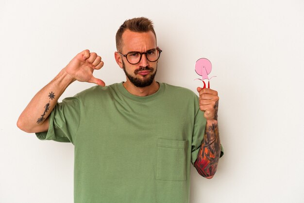 Junger kaukasischer Mann mit Tätowierungen, die Lutscher einzeln auf weißem Hintergrund halten, fühlt sich stolz und selbstbewusst, Beispiel zu folgen.