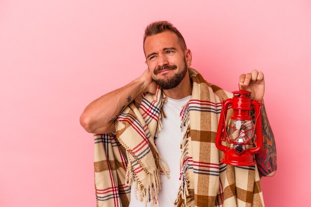 Junger kaukasischer Mann mit Tätowierungen, die Vintage-Laterne einzeln auf rosafarbenem Hintergrund halten, den Hinterkopf berühren, nachdenken und eine Wahl treffen.