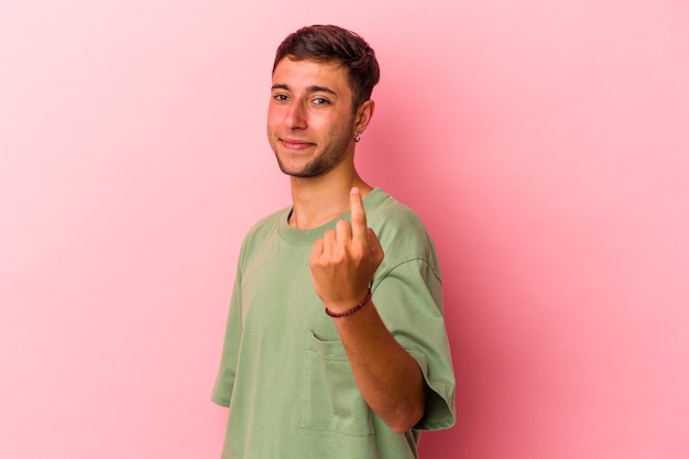 Junger kaukasischer Mann mit Tätowierungen einzeln auf gelbem Hintergrund, der mit dem Finger auf Sie zeigt, als ob er einladen würde, näher zu kommen.