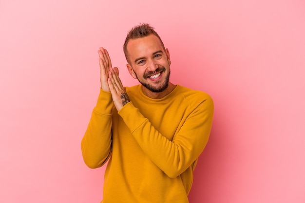 Junger kaukasischer Mann mit Tätowierungen einzeln auf rosafarbenem Hintergrund, der sich energisch und bequem fühlt und sich die Hände selbstbewusst reibt.