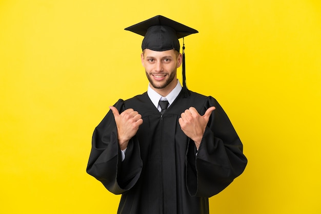 Junger kaukasischer Mann mit Universitätsabsolvent isoliert auf gelbem Hintergrund mit Daumen nach oben Geste und lächelnd