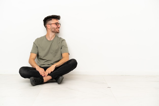Junger kaukasischer Mann sitzt auf dem Boden isoliert auf weißem Hintergrund in Seitenlage