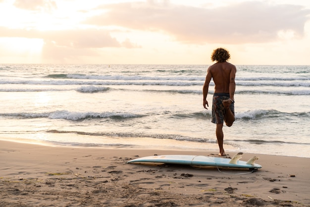 Junger kaukasischer Mann steht früh auf, um bei Sonnenaufgang zu surfen