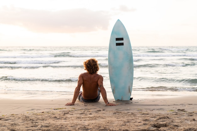 Junger kaukasischer Mann steht früh auf, um bei Sonnenaufgang zu surfen