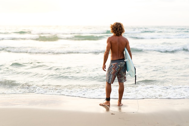 Junger kaukasischer Mann steht früh auf, um bei Sonnenaufgang zu surfen