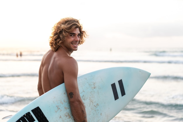 Junger kaukasischer Mann steht früh auf, um bei Sonnenaufgang zu surfen